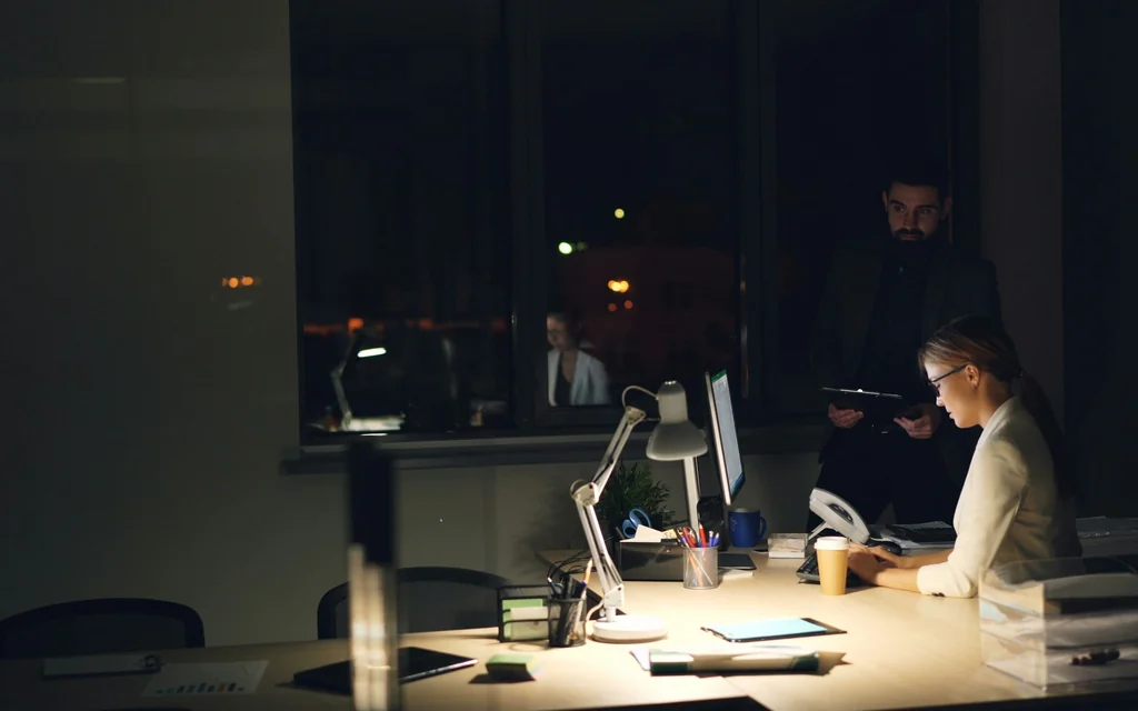 Zwei Mitarbeitende arbeiten spätabends an einem beleuchteten Arbeitsplatz im dunklen Büro