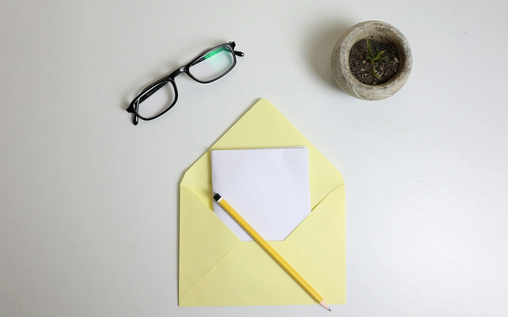Geöffneter Briefumschlag mit einem Blatt, Bleistift und Brille auf einem Tisch