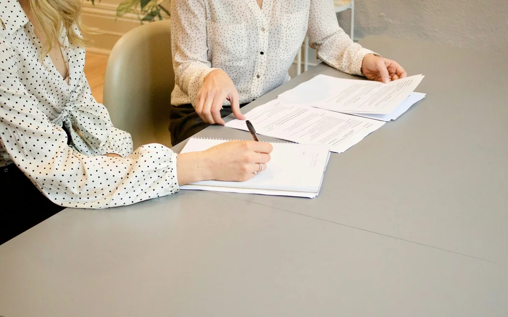 Zwei Personen gehen am Tisch gemeinsam Unterlagen durch und machen Notizen